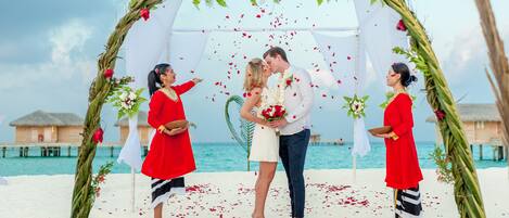 A wedding ceremony on a beach with a white canopy and floral decorations.