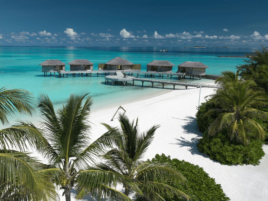 Overwater bungalows connected by a pier, a white sandy beach, and clear turquoise waters.