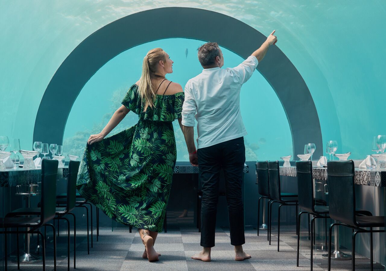 A couple walking towards a dining area with tables set for a meal.