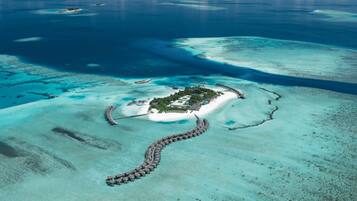 Overwater bungalows connect to a serene beach and turquoise lagoon via a winding pathway.