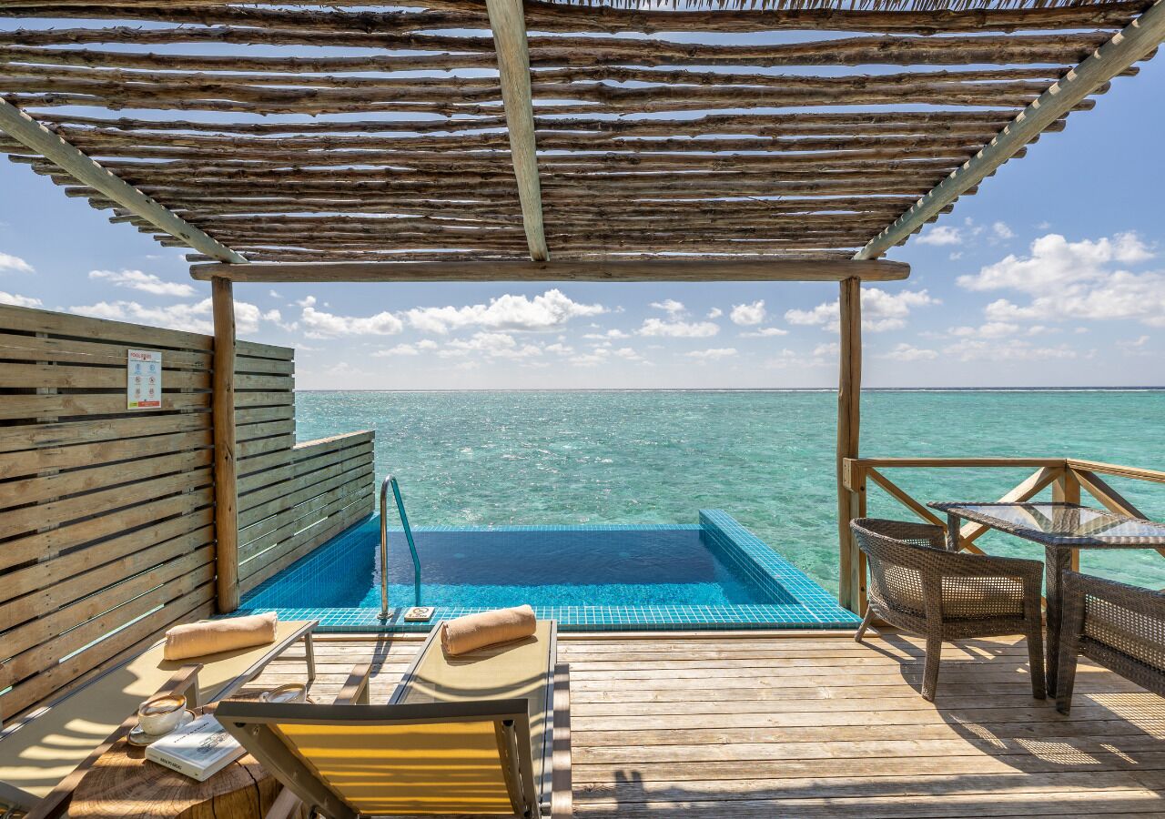 Una terraza de madera con una piscina pequeña, sillas de descanso y una mesa con vistas al mar.