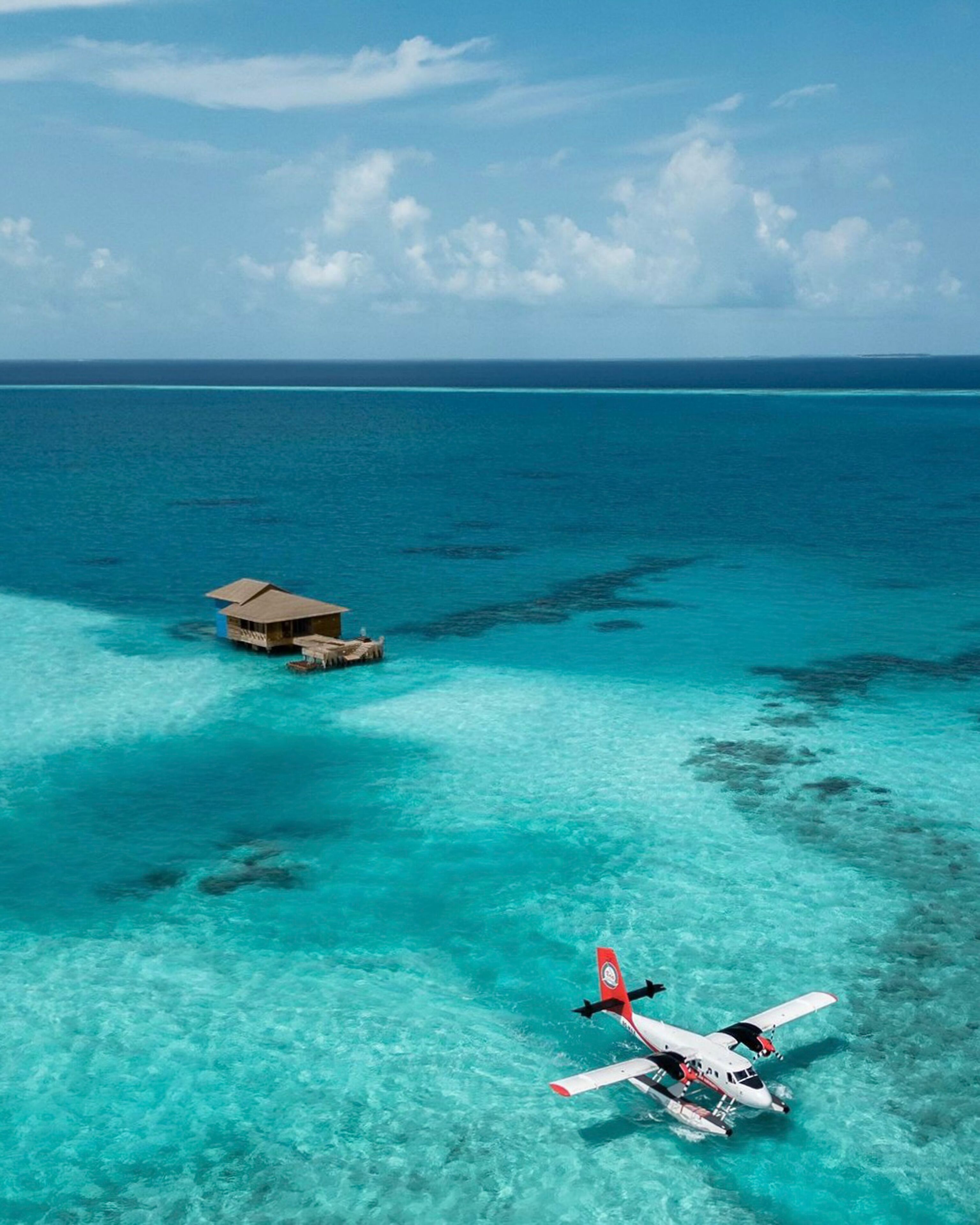 Uma cabana sobre a água com vista clara do oceano e um hidroavião na água.