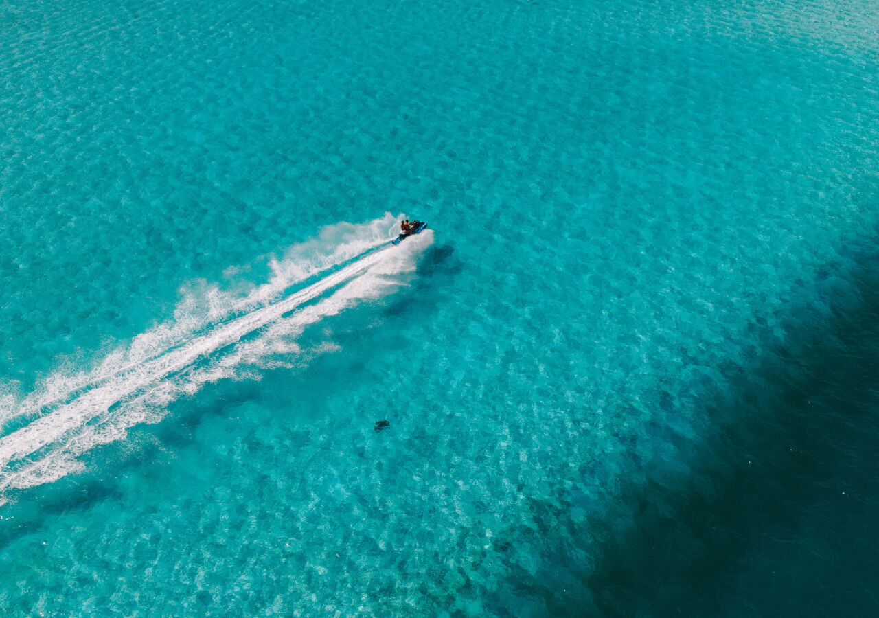 Eine Vogelperspektive auf ein klares türkisblaues Meer, wobei ein Jetski eine Bugwelle verursacht.