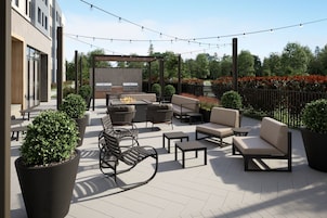 Un patio al aire libre con mobiliario, una parrilla y luces colgantes.