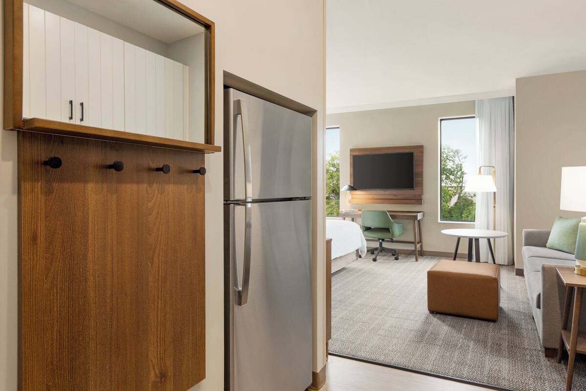 A hotel room with a kitchenette, a bed, a TV, a desk, and a sofa.