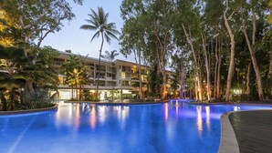 A large, illuminated swimming pool surrounded by trees and a hotel building. - Lxry 2 bed Apt-Sea and Mountain View (Palm Cove)