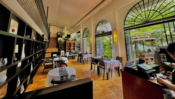 Un restaurante espacioso con techos altos, ventanas grandes y diversas opciones de asientos, incluyendo mesas y sillas.