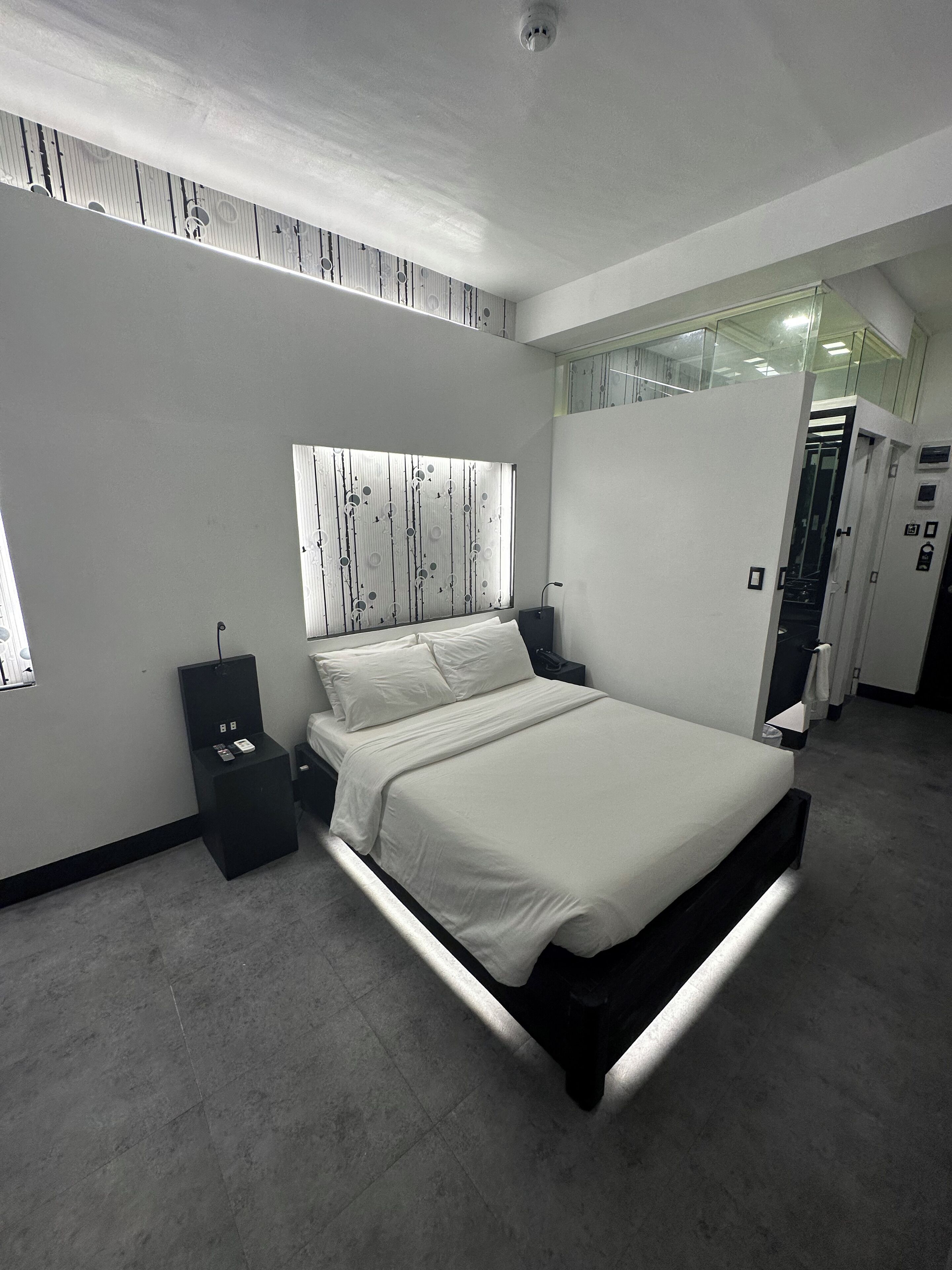 A modern bedroom with a large bed, a bedside table, a nightstand, and a window with blinds.