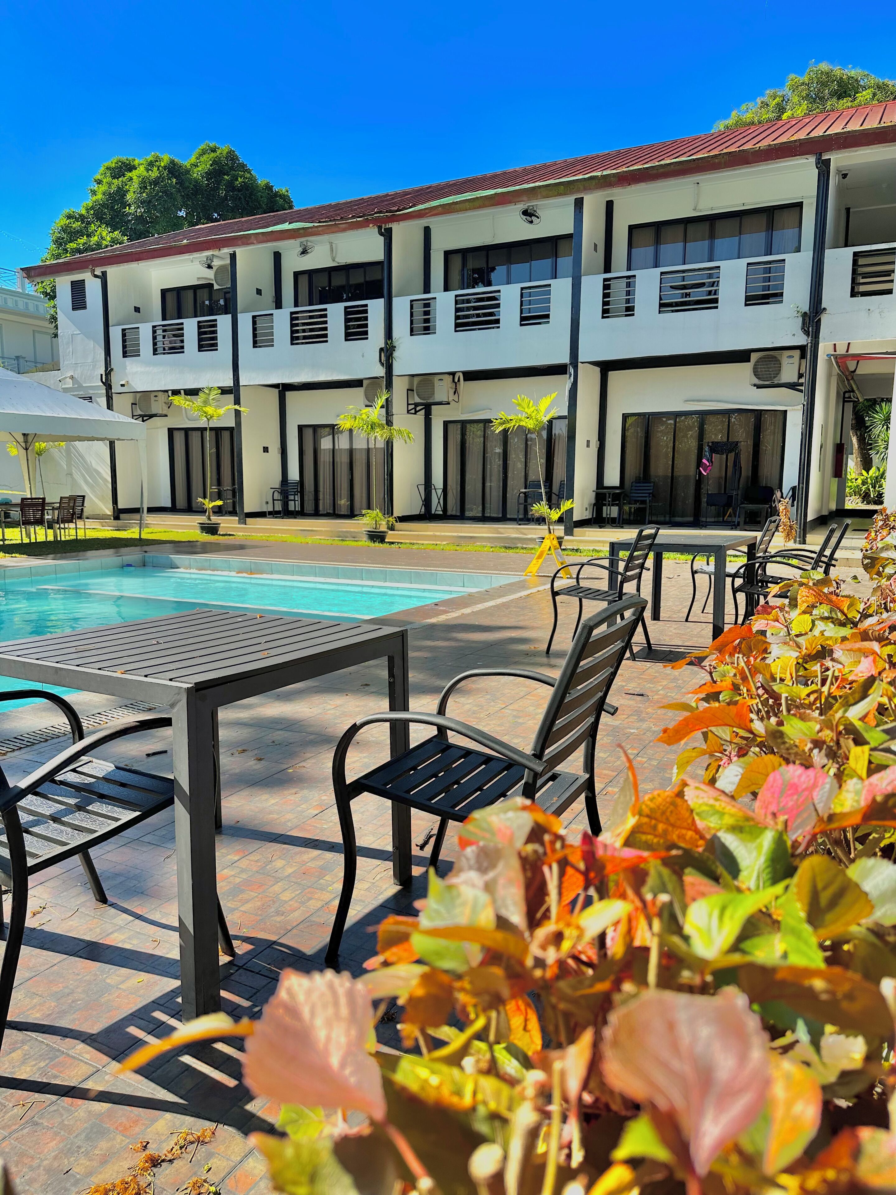 Zona de piscina con sillones y mesas, rodeada por un edificio de varios pisos y balcones.