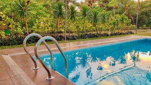 Una piscina con barandales metálicos, rodeada de vegetación exuberante y un deck de baldosas.