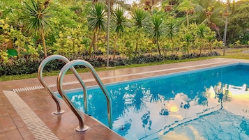 Una piscina con barandales metálicos, rodeada de vegetación exuberante y un deck de baldosas.