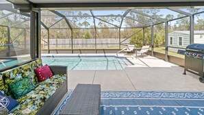Un espace extérieur abrité comprenant une piscine, un barbecue et un coin salon avec un canapé et des fauteuils.