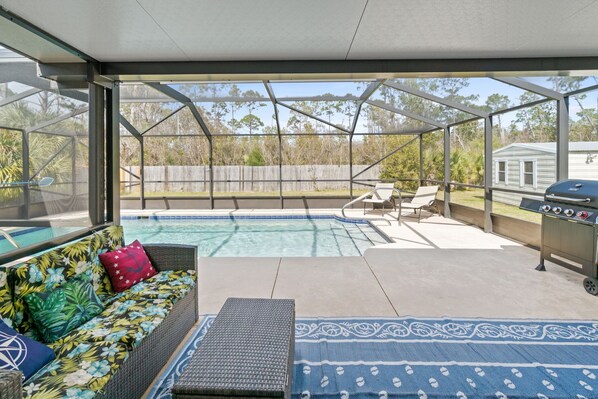 A covered outdoor area with a pool, a grill, and a seating area with a sofa and chairs.