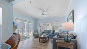 Un salon spacieux doté d’un ventilateur de plafond, d’un canapé bleu, d’une table basse en bois et d’un fauteuil en osier.