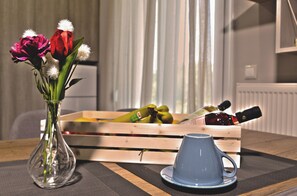 Una mesa de madera con un jarrón de cristal que contiene flores, una taza azul y un cesto de madera con frutas y una botella.