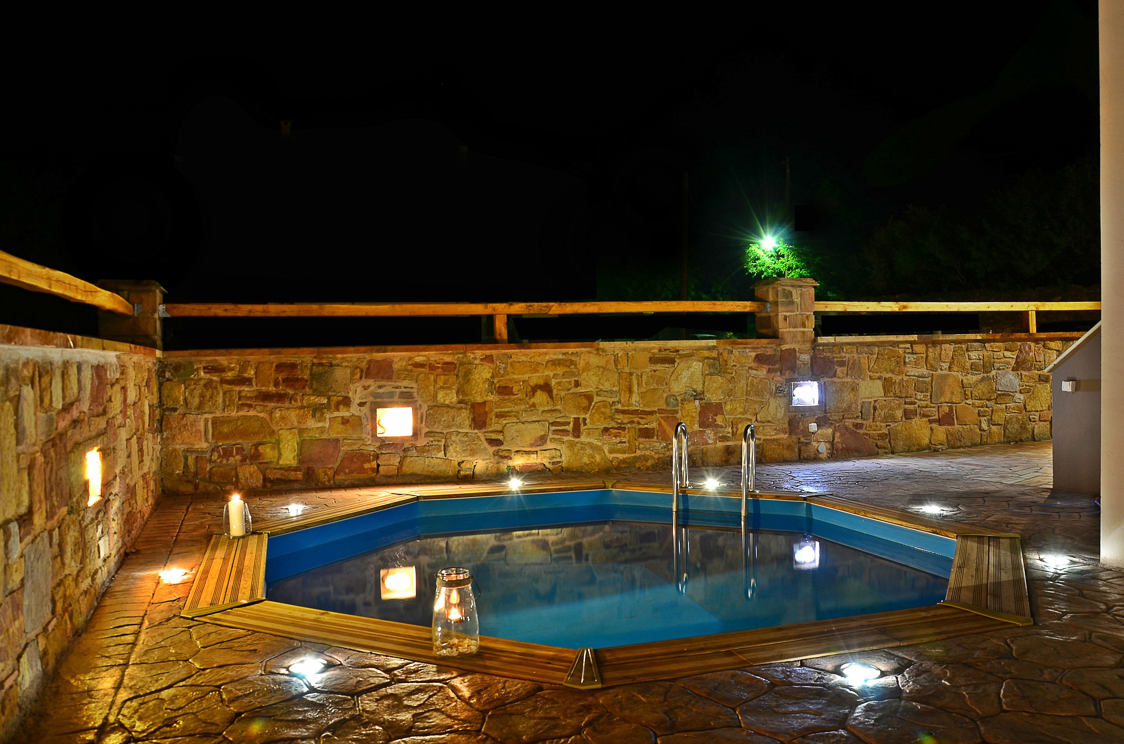 A stone-walled outdoor swimming pool with a wooden deck and a stone wall on one side.