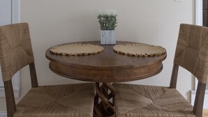 Ein Essbereich mit einem runden Holztisch, zwei Korbstühlen, einer rustikalen Metalluhr und einem kleinen Topfpflanzen.
