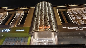 A modern building with a prominent cylindrical tower, illuminated signage, and a facade featuring geometric patterns. - Brzeen Hotel - Riyadh - فندق برزين الرياض (Riyadh)