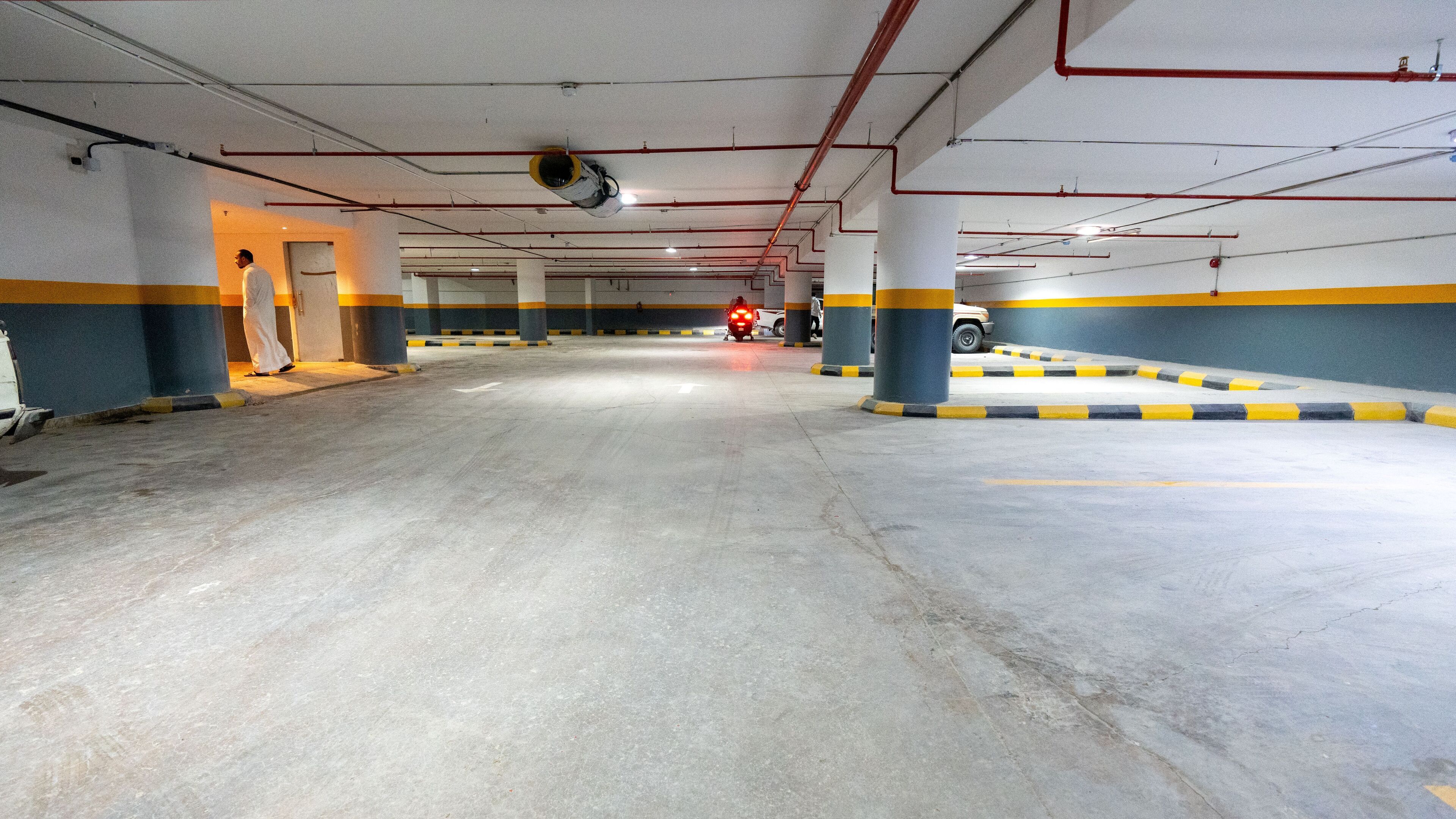 An indoor parking garage with concrete floors, yellow and blue painted walls, and red pipes on the ceiling.