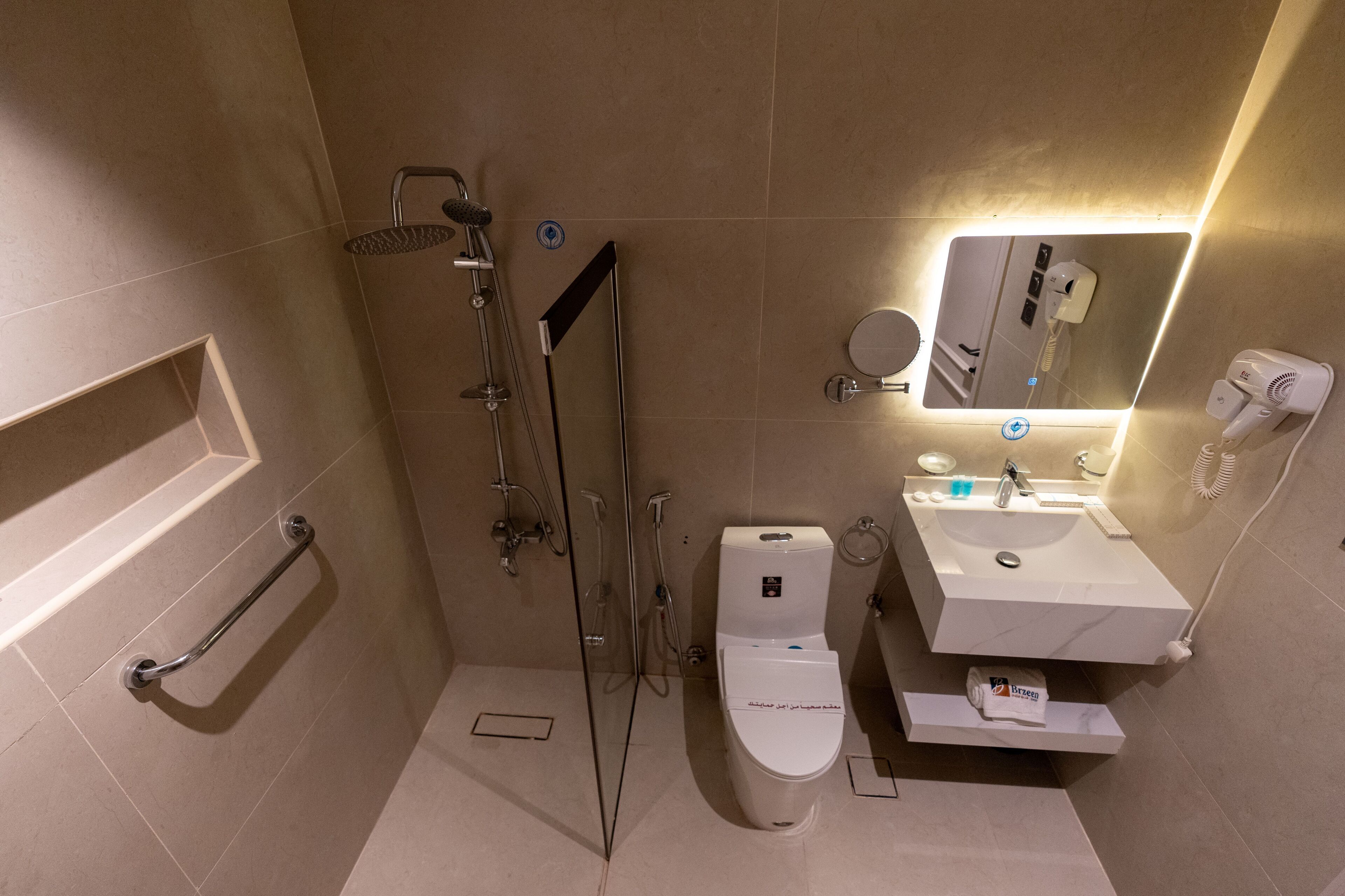 Un baño moderno con cabina de ducha de vidrio, inodoro, lavabo con espejo y secador de pelo.