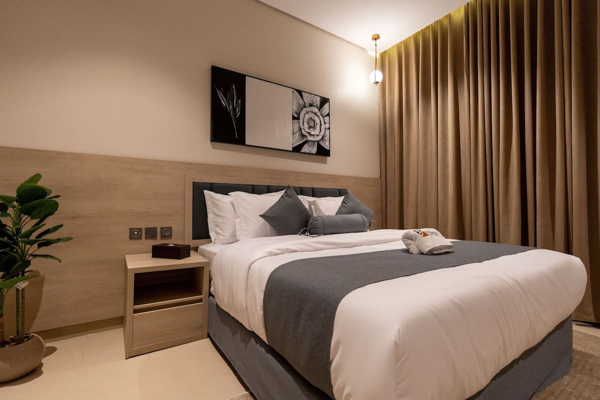Una habitación de hotel moderna con una cama grande, una mesita de noche, una planta en maceta y una obra de arte colgada en la pared.
