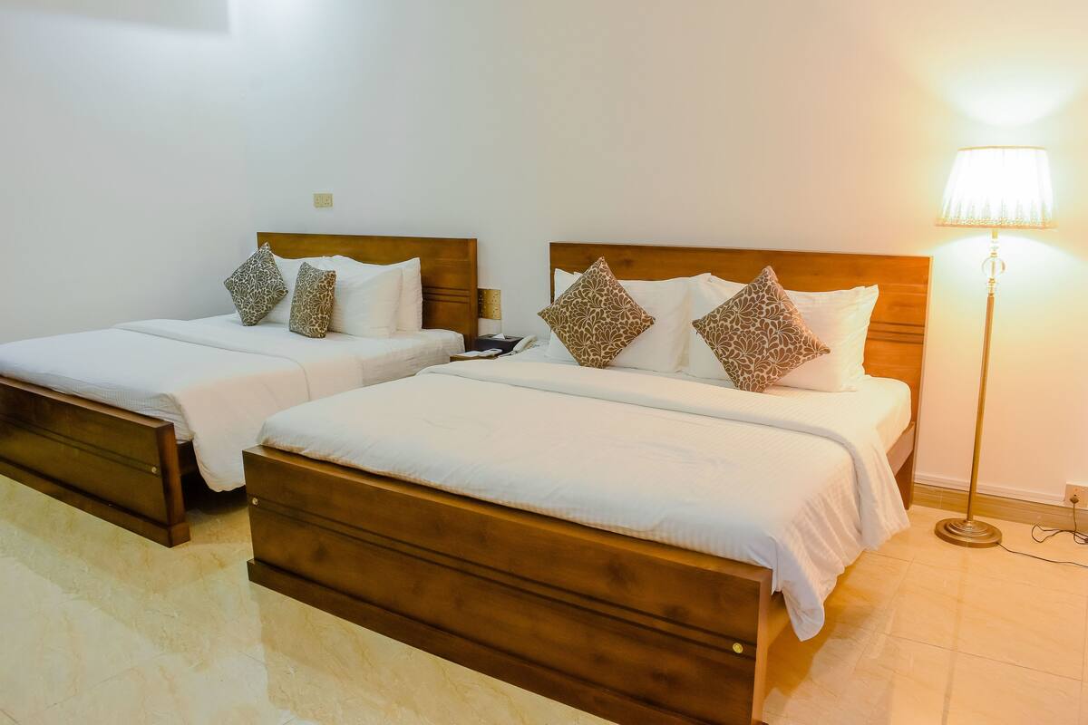 Two single beds with wooden headboards, white bedding, patterned pillows, a bedside table, and a floor lamp.