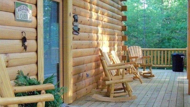 Een houten chalet met een veranda, schommelstoelen en een bord met een welkomstboodschap.