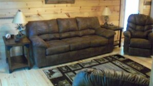 Een gezellige woonkamer met een bruine leren bank, een bijpassende fauteuil en een kamerbreed tapijt met dessin.