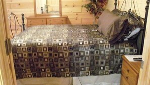 Een slaapkamer met een bed met een patroongordijn, een houten dressoir en een nachtkastje.