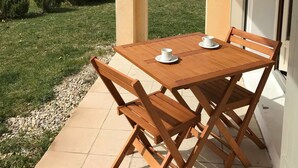 A wooden table and chairs on a balcony with a view of buildings and a hill. - Résidences La Tour du Guet (Montbrun-les-Bains)