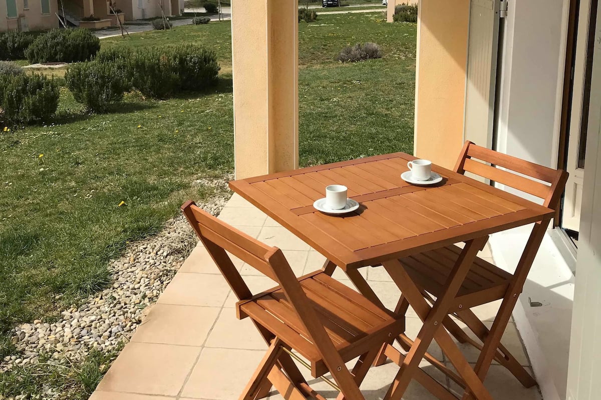 A wooden table and chairs on a balcony with a view of buildings and a hill.