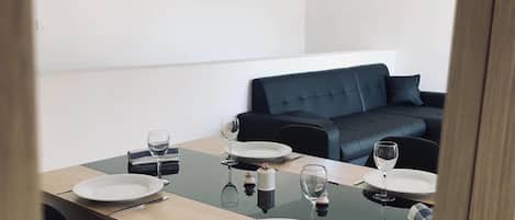 Un comedor con una mesa de madera dispuesta para cuatro personas, sillas negras y un sofá negro al fondo.