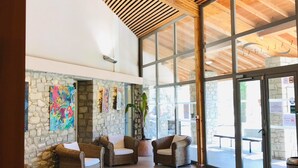 A spacious lobby with a high ceiling, stone walls, and large windows. There are wicker chairs and a glass display case with towels. - Résidences La Tour du Guet (Montbrun-les-Bains)