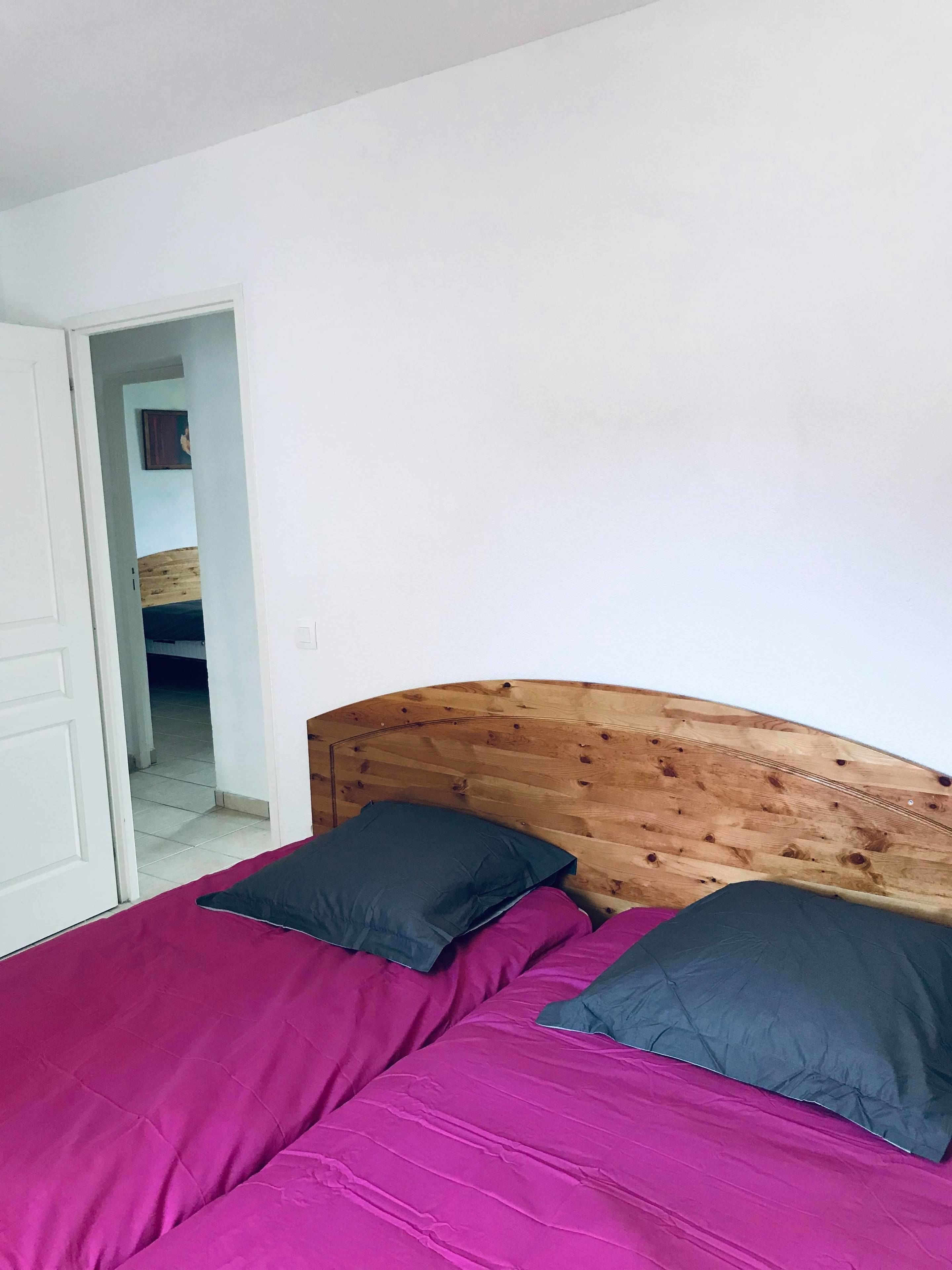 A room with a bed featuring a wooden headboard, two pillows, and a bright pink bedspread.