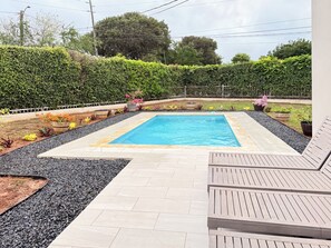 Una piscina rectangular con un bordeado de baldosas, rodeada por un seto bajo y grava.