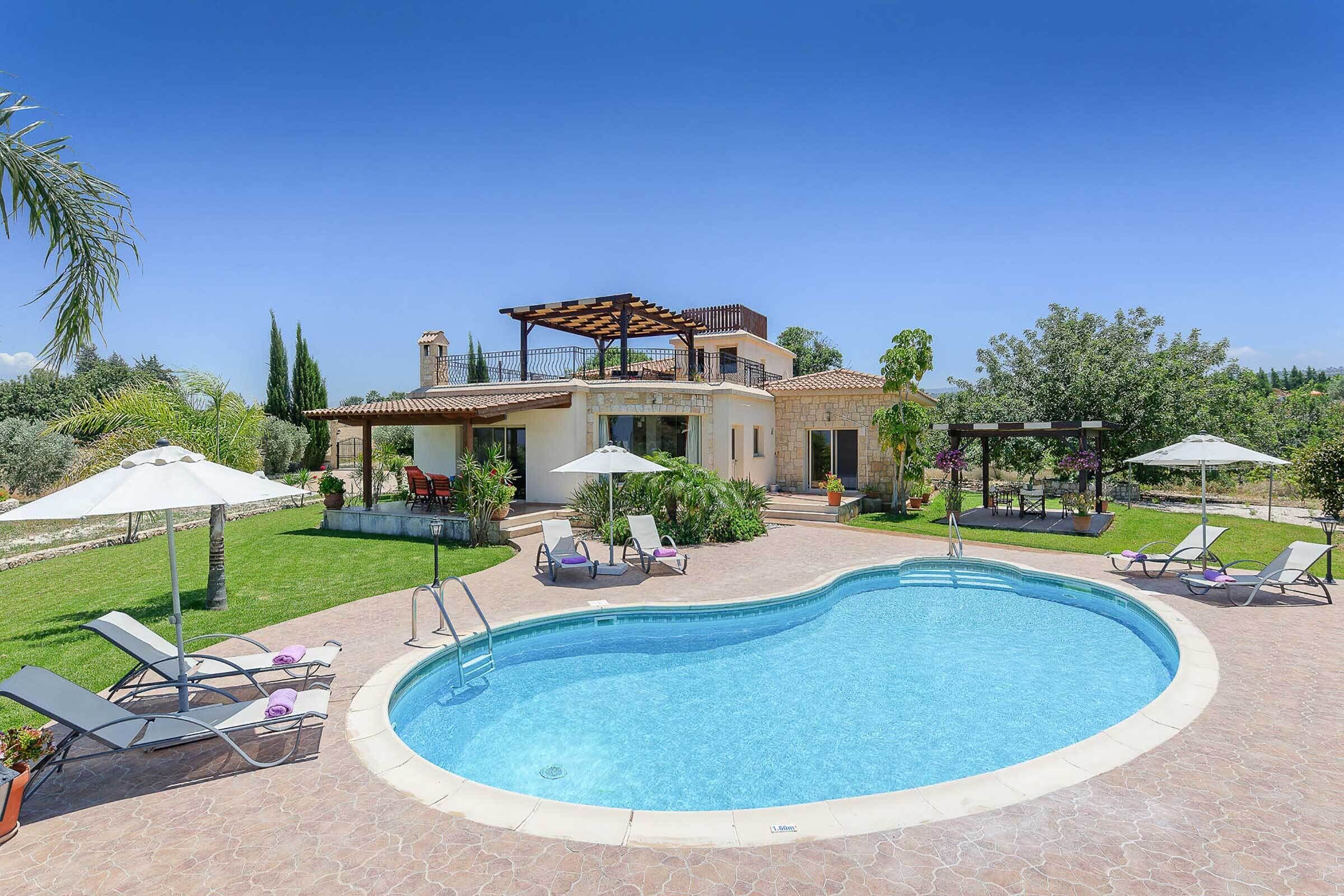 Una piscina con sillas de descanso y sombrillas, rodeada de un césped cuidado y una casa con balcón.