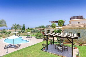 A backyard with a swimming pool, outdoor seating, and a pergola. - Villa Yialos (Neo Chorio)