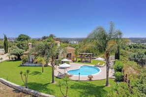 A private pool area with a stone deck, lounge chairs, and umbrellas. - Villa Yialos (Neo Chorio)