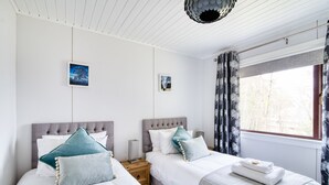 A bedroom with two beds, a window with curtains, and a ceiling light fixture. - Otter With Mountain View and Enclosed Decking (Crianlarich)