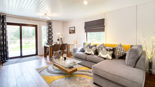 A modern living room with a glass coffee table, grey sofa, and a yellow rug. - Otter With Mountain View and Enclosed Decking (Crianlarich)