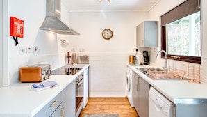 A compact kitchen with a stainless steel range hood, a clock, a washing machine, and a toaster. - Otter With Mountain View and Enclosed Decking (Crianlarich)