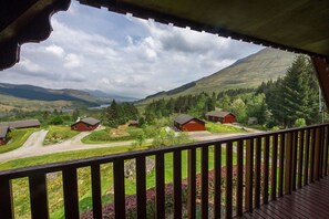 A view from a balcony overlooking a rural landscape with several red-roofed cabins and a lake in the distance. - Beautiful 5 Star Chalet With Sauna and spa Bath (Crianlarich)
