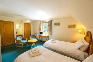 Ein Hotelzimmer mit zwei Betten, einem Schreibtisch mit Computer, einem Stuhl und einem Fenster mit Vorhängen.