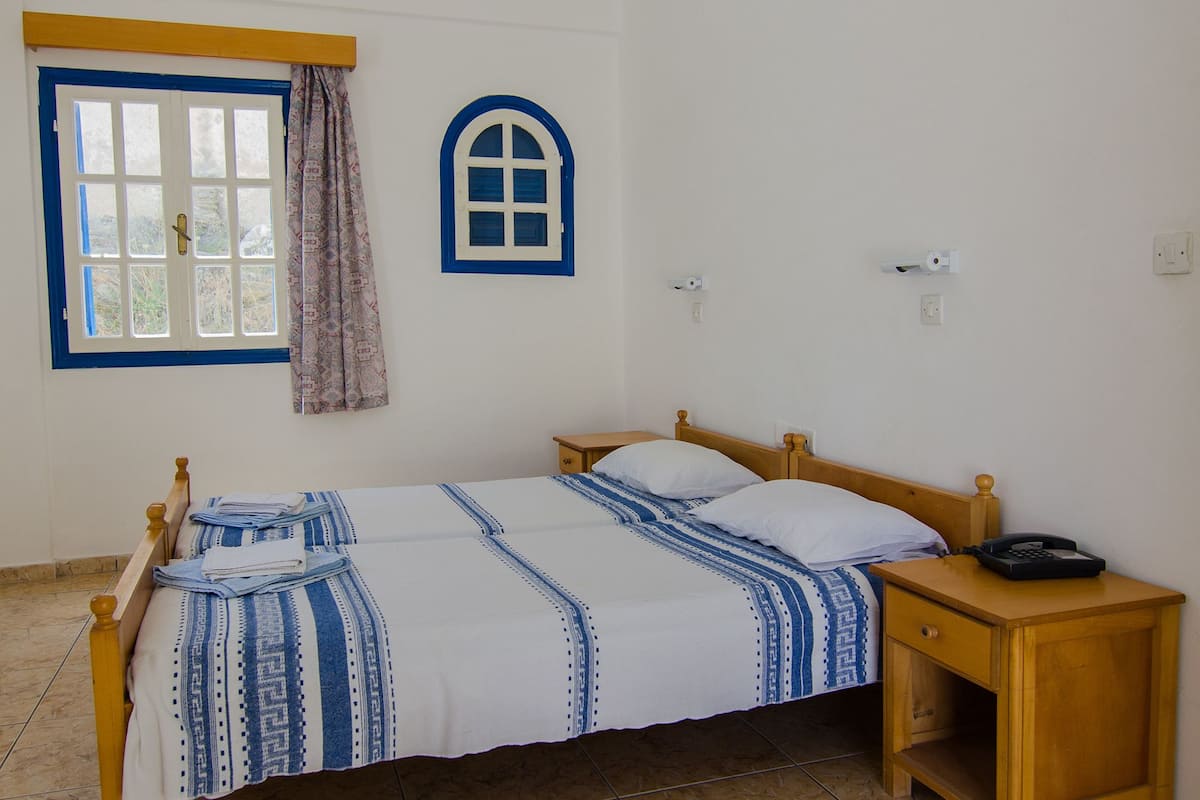 A bedroom with a bed, a nightstand, a window with curtains, a ceiling fan, and a wall-mounted light switch.
