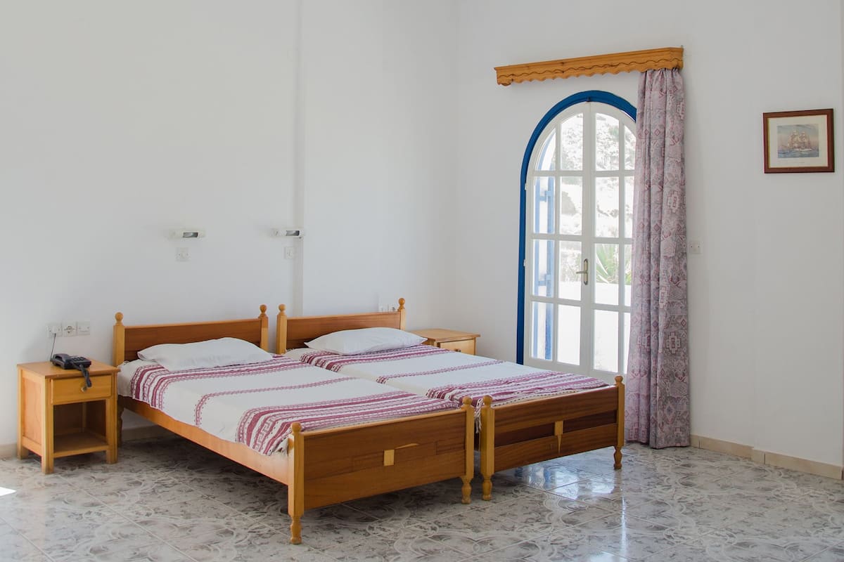 A bedroom with a wooden bed, a nightstand, a window with blue trim, and a ceiling fan.