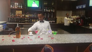 A bar area with a bartender preparing drinks, shelves of liquor bottles, and a television displaying a sports event. - Lan Tian International Hotel (Addis Ababa)