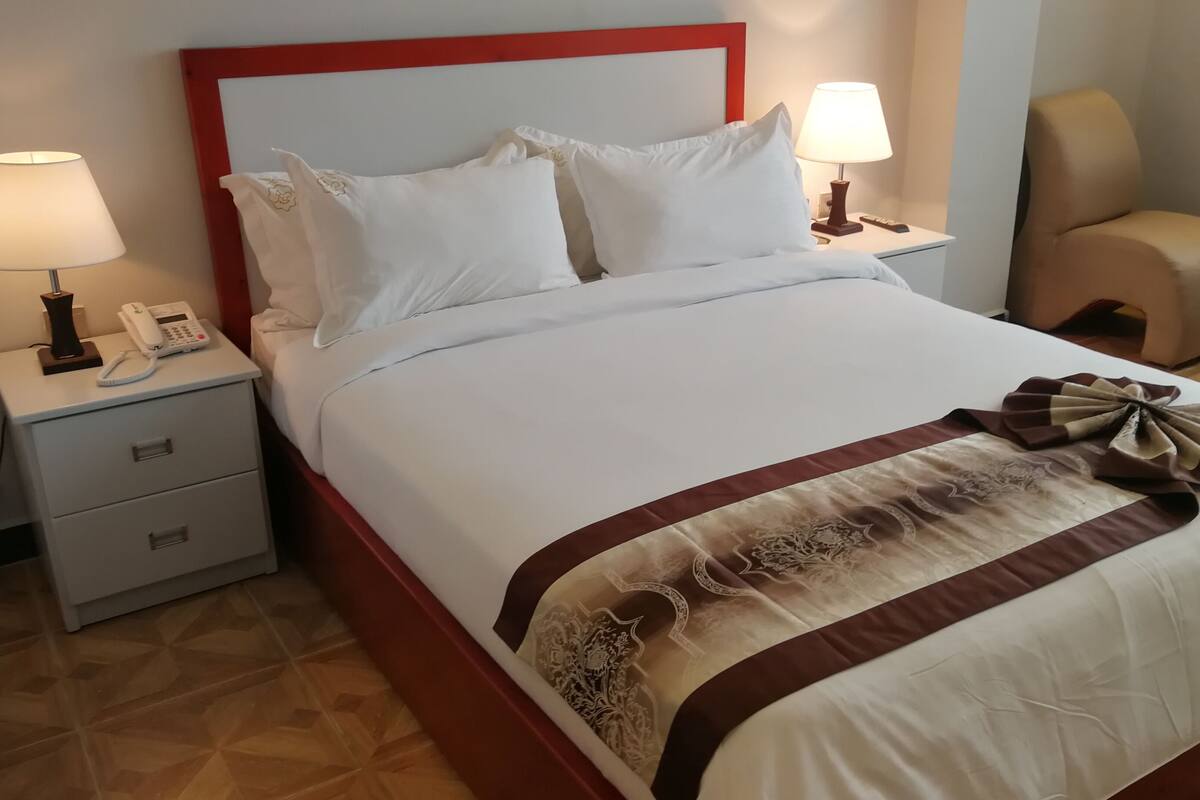 A hotel room with a neatly made bed, two bedside lamps, a telephone, and a chair.