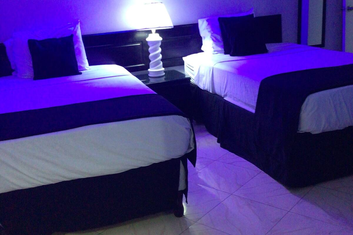 Habitación de hotel con dos camas, una mesita de noche con lámpara y una lámpara en el techo.