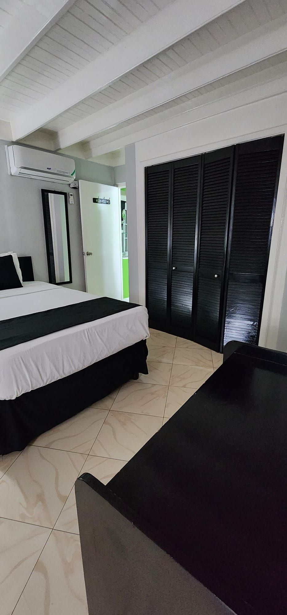 A hotel room with a bed, a desk, a wardrobe, and an air conditioning unit.