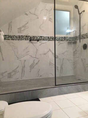 A bathroom with a glass-enclosed shower, white marble walls, and a tiled floor.